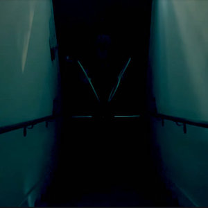 The Moon single art. A dark stairwell with a faint glimpse of a person holding 8 rings.